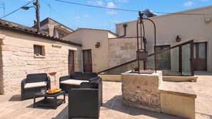 Un patio al aire libre con mobiliario de mimbre, una mesa de piedra y vistas de los edificios circundantes.