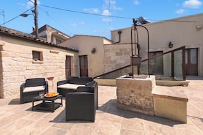 Un patio al aire libre con mobiliario de mimbre, una mesa de piedra y vistas de los edificios circundantes.