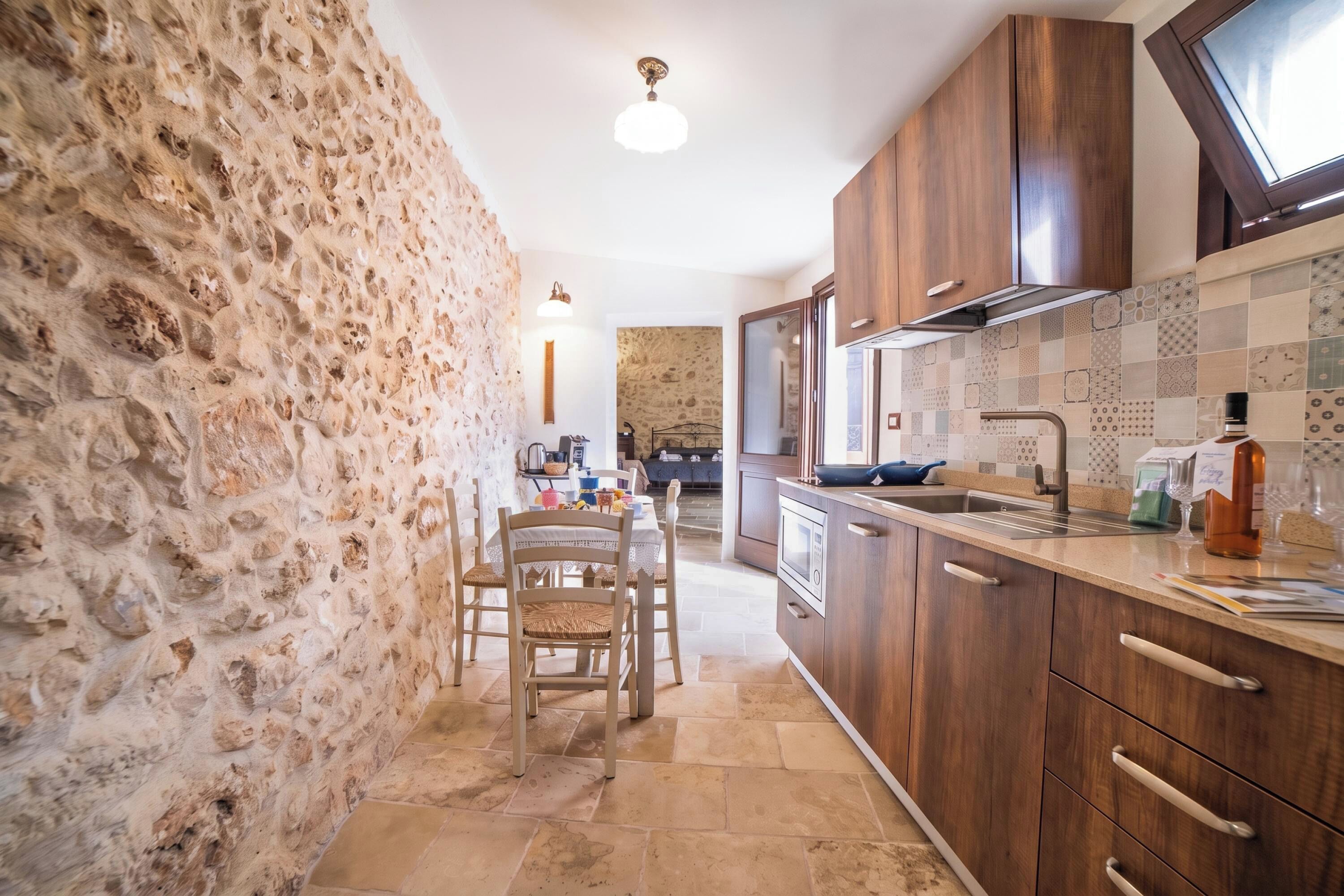 Una cocina con paredes de piedra, armarios de madera, una zona de comedor con sillas y un salpicadero de azulejos.