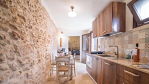 Una cocina con paredes de piedra, armarios de madera, una zona de comedor con sillas y un salpicadero de azulejos.