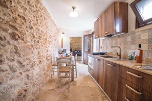 Una cocina con paredes de piedra, armarios de madera, una zona de comedor con sillas y un salpicadero de azulejos.