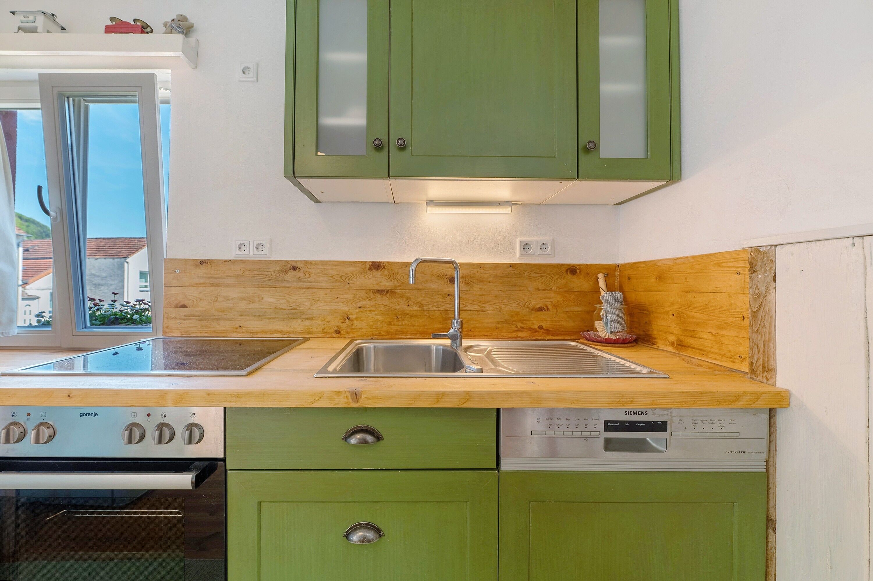 Eine Küche mit grünen Schränken, einer Holz Arbeitsplatte, einem Spülbecken, einem Geschirrspüler und einem Backofen.