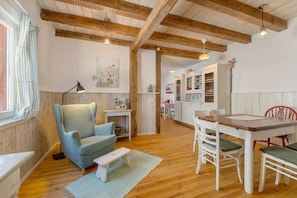 Un'accogliente stanza con soffitto in legno, un tavolo da pranzo con sedie, un divano e un piccolo tavolino con una lampada.