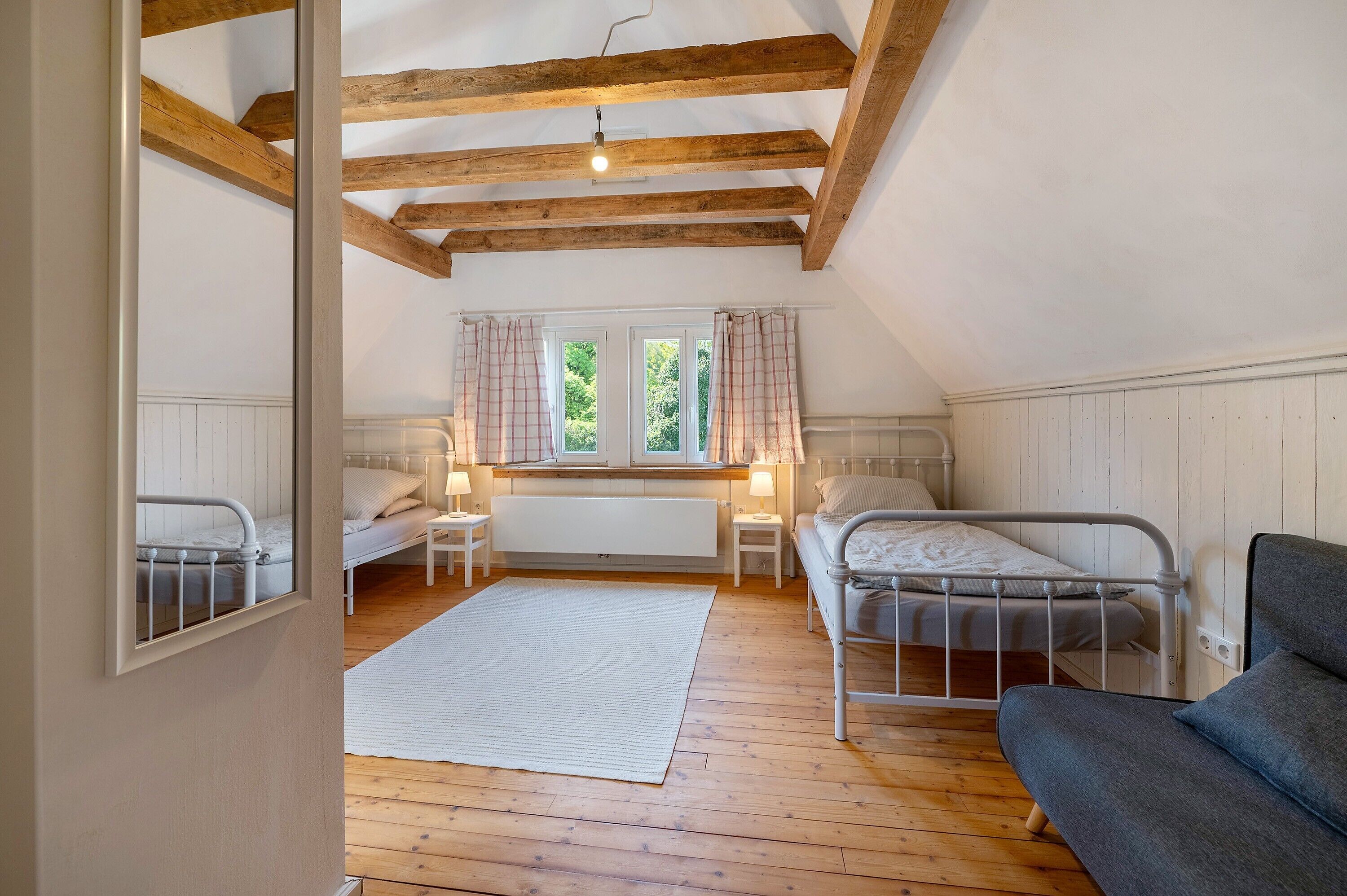 A bedroom with two beds, a window with curtains, a radiator, and a wooden ceiling.