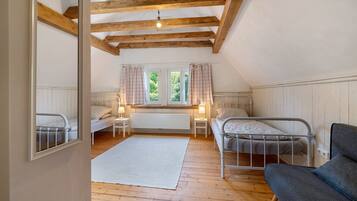 A bedroom with two beds, a window with curtains, a radiator, and a wooden ceiling.