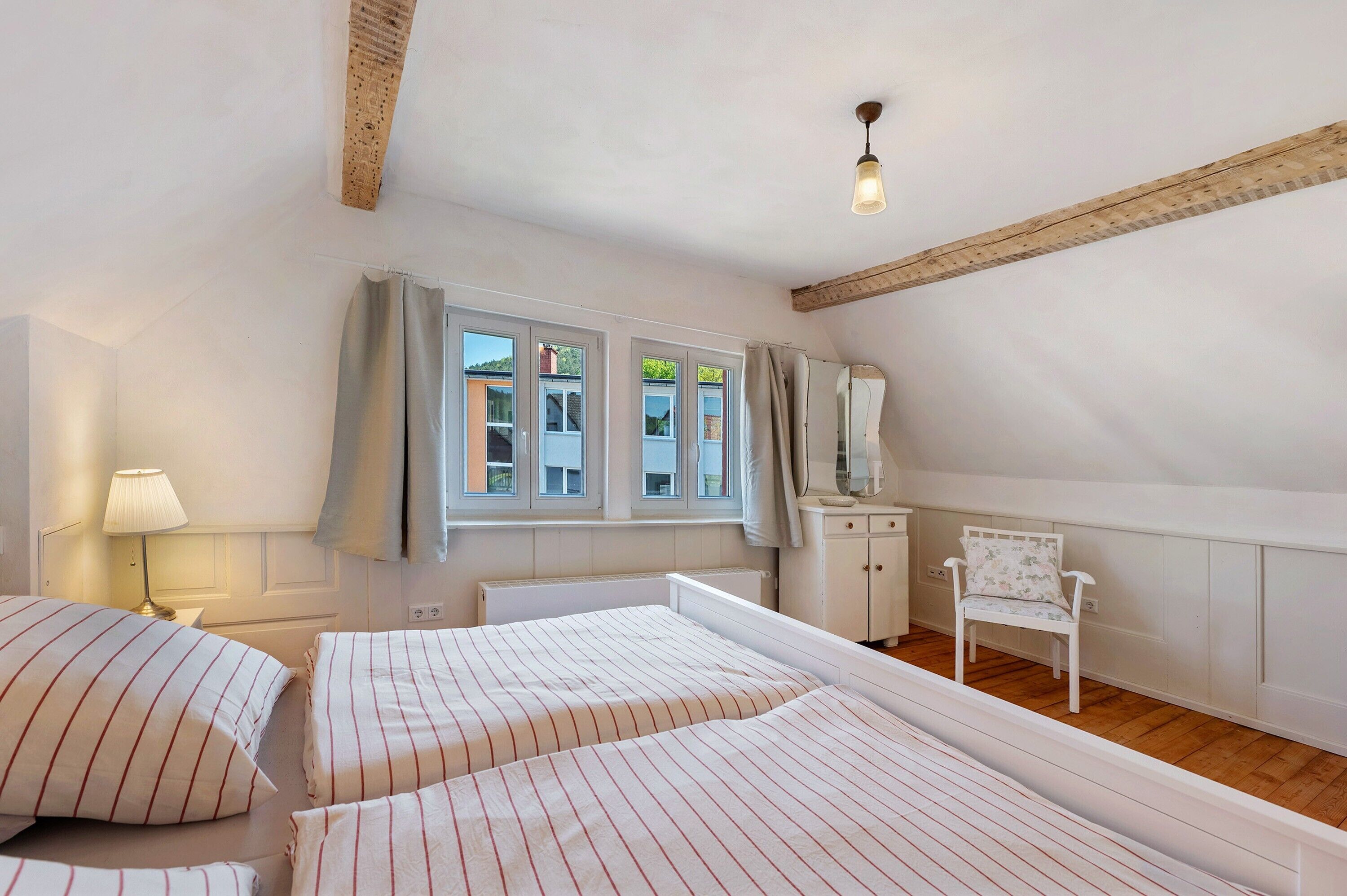 Une chambre avec deux lits, une chaise, une lampe et une fenêtre avec des rideaux.