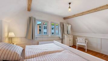 Une chambre avec deux lits, une chaise, une lampe et une fenêtre avec des rideaux.