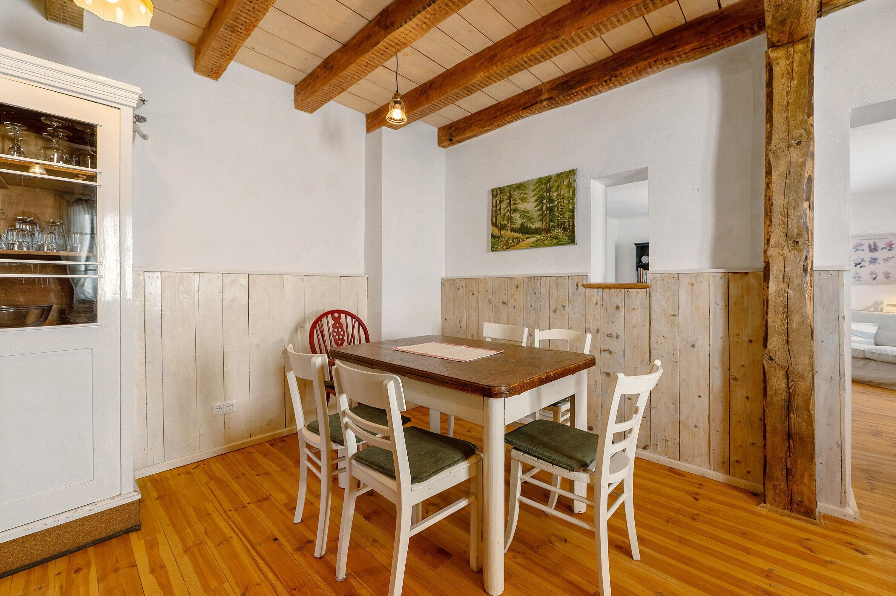 A dining area with a wooden table and chairs, a wooden ceiling, and a white cabinet with glass doors.