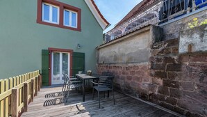 En träveranda med ett bord och stolar, en grön dörr och en mur av tegelsten.