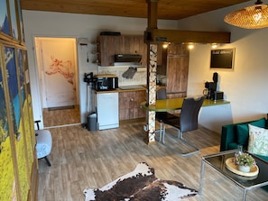 Una cocina moderna equipada con microondas, estufa y cafetera. Hay un comedor con mesa y sillas. El espacio tiene piso de madera y un tapete de cuero de vaca.