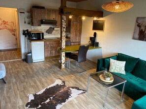 Un espacio habitable compacto con kitchenette, zona de comedor, sofá verde y alfombra de cuero de vaca.