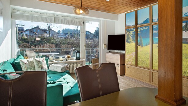 A modern living room with a large window, a dining area, and a television.