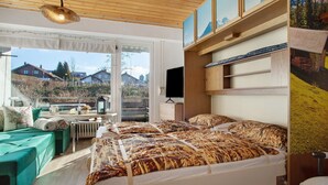 A bedroom with a bed, a desk, and a view of the outside.