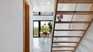 Un interior moderno con una escalera de madera, un comedor con mesa y sillas, y vistas al exterior.