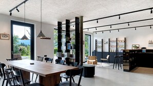 Un interior moderno con una larga mesa de madera, sillas negras, una estantería y una zona de bar.
