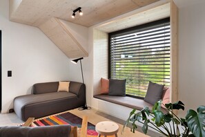 En moderne stue med sofa, bænk ved et vindue, gulvlampe og et farverigt tæppe.