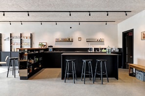 A modern bar area with a central island, stools, shelves with bottles, and a bench.