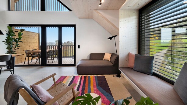 Ein modernes Wohnzimmer mit einer Couch, einem Essbereich und einem großen Fenster mit Jalousien.