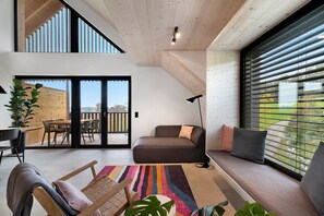 A modern living room with a sofa, a dining area, and a large window with blinds. - Apartment 'Noir' with Mountain View, Balcony, and Wi-Fi (Sigmarszell)
