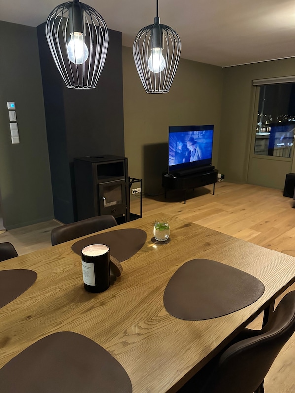 Una sala de estar moderna con una mesa de comedor de madera, dos lámparas colgantes, un televisor y una chimenea.