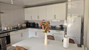 Una cocina moderna con armarios blancos, encimera blanca, un jarrón con flores y un adorno con forma de corazón en la mesa.