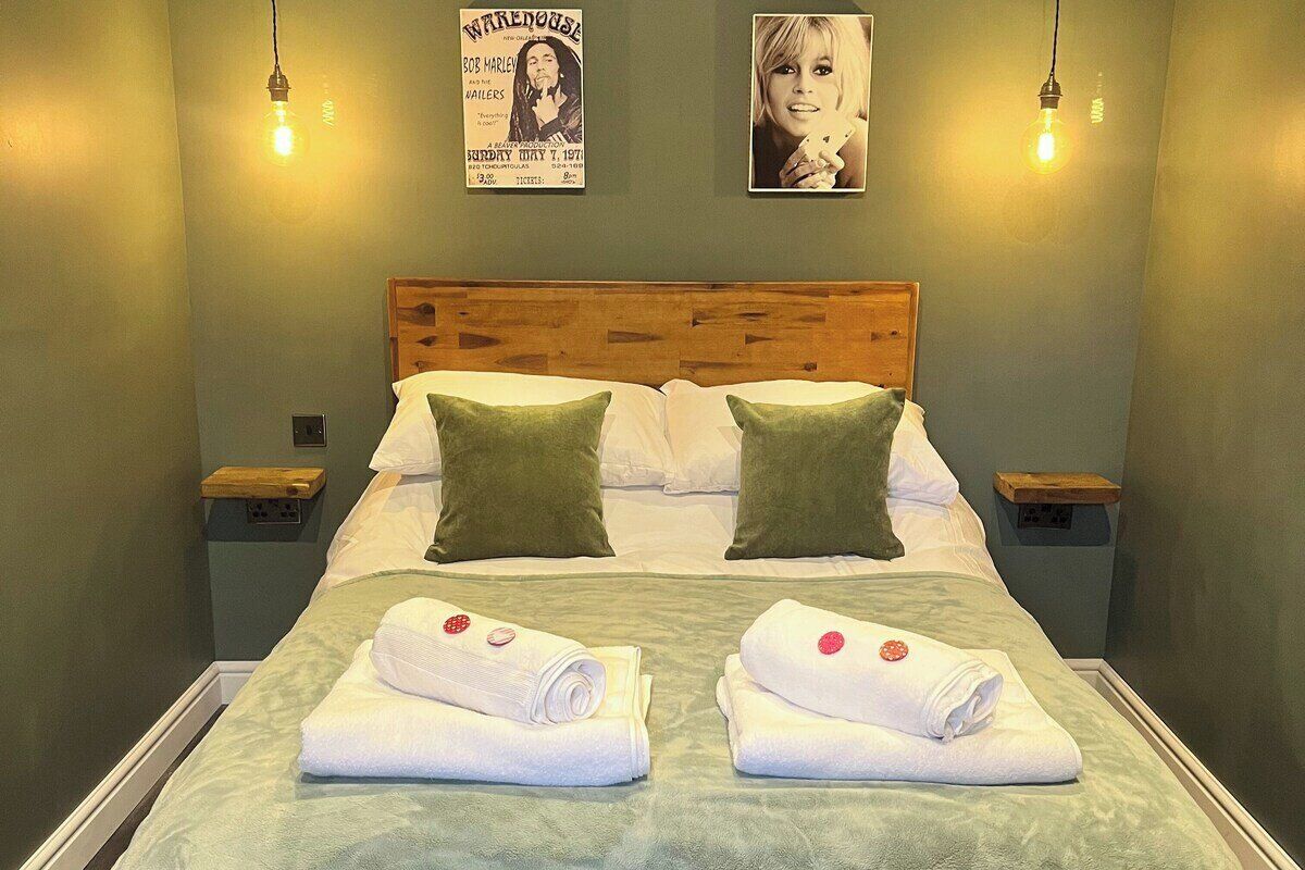 A neatly made bed with two pillows, two rolled towels, and a poster on the wall.