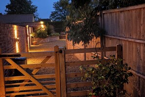 A wooden gate leading to a gravel area with a brick wall and a wooden fence.