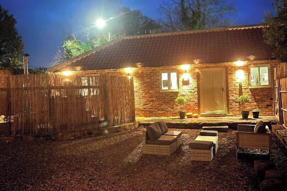 A rustic stone building with a wooden door, a small porch with seating, and a wooden fence.
