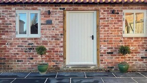 A brick building with a white door, two windows, and two potted plants.