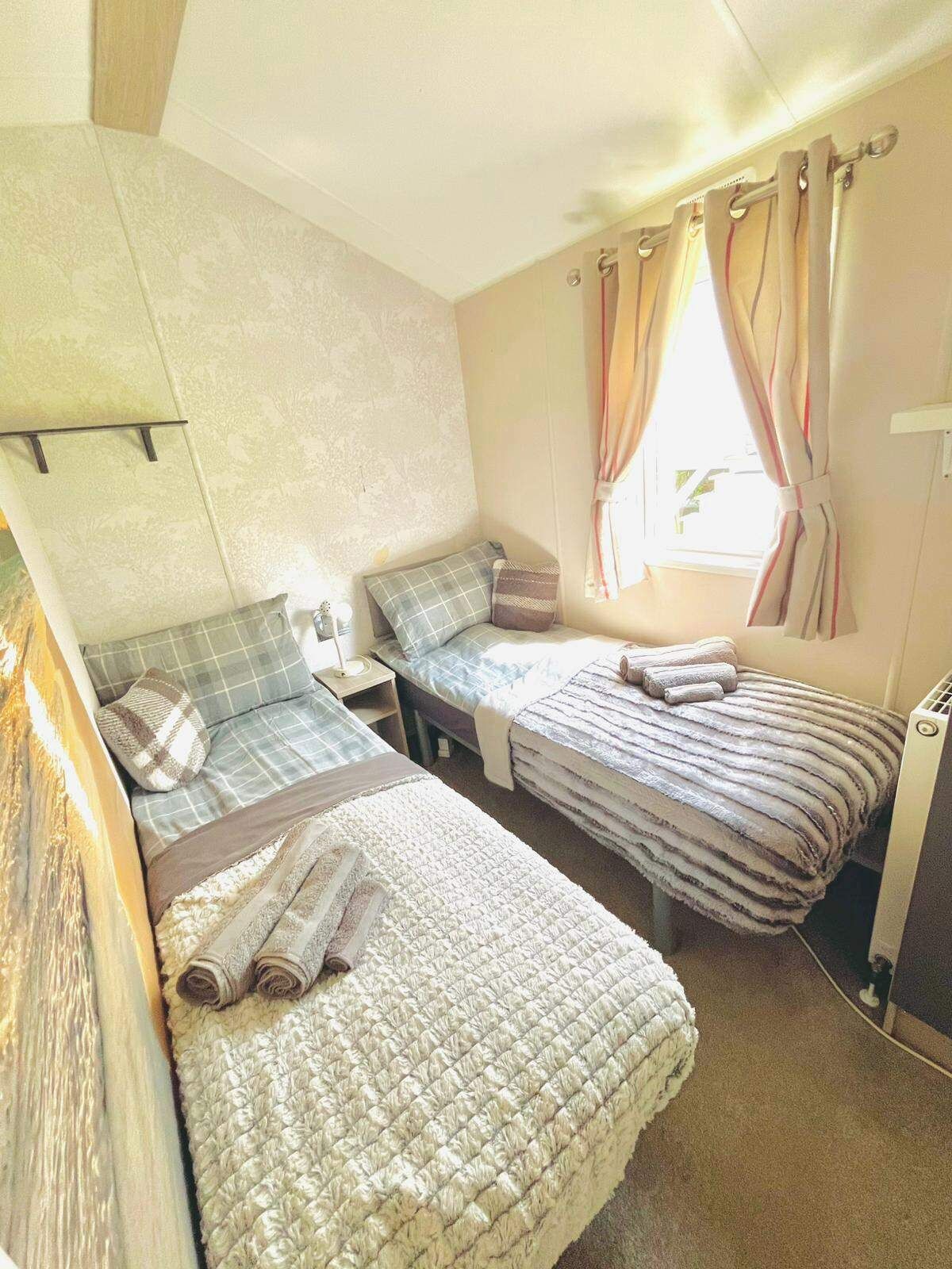A room with two beds, a nightstand, a lamp, and a window with curtains.