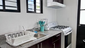 Uma cozinha compacta com fogão a gás, forno embutido, pia e janela com persianas.