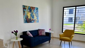 Uma sala de estar moderna com um sofá azul escuro, uma poltrona amarela e um quadro abstrato colorido na parede.