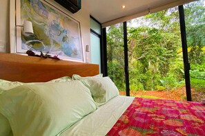 A bed with white linens, a colorful blanket, and a painting above it.