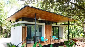 Una casa moderna con terraza de madera, ventanas amplias y balcón con sillas azules.