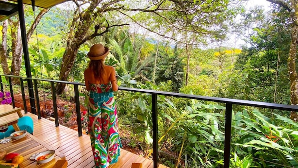 Una persona de pie sobre una terraza de madera, con vistas a un paisaje verde y exuberante.