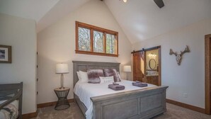 Een slaapkamer met een groot bed, een raam, een deur en een spiegel aan de muur.