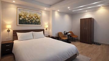 Ein Hotelzimmer mit einem großen Bett, zwei Nachttischen, einem Schreibtisch mit Stühlen, einem Kleiderschrank und einem Bild an der Wand.