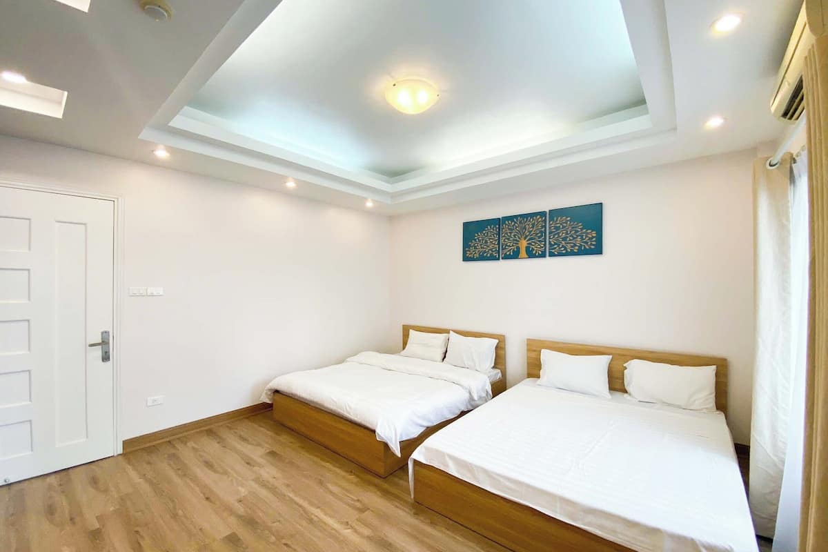 Une chambre avec deux lits, un luminaire au plafond et une œuvre d’art accrochée au mur.