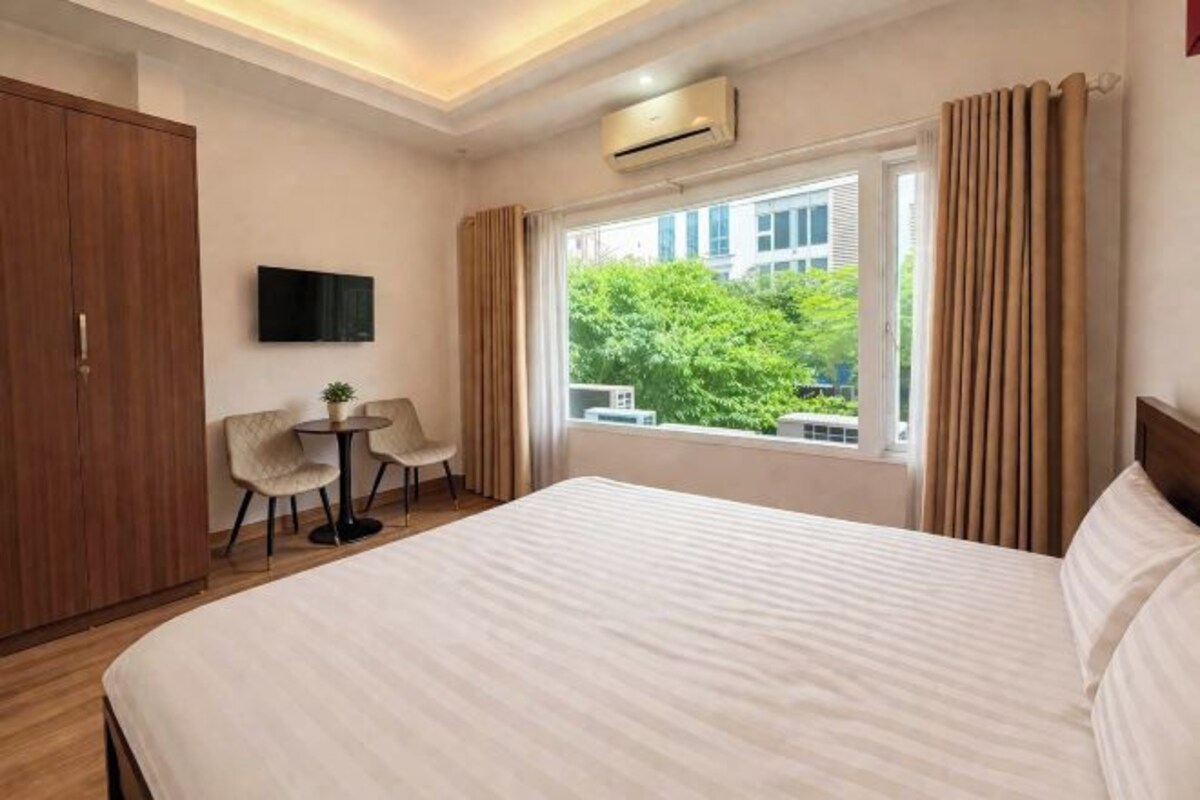 Ein Hotelzimmer mit Bett, Fernseher, kleinem Tisch mit Stühlen und einem Fenster mit Vorhängen.