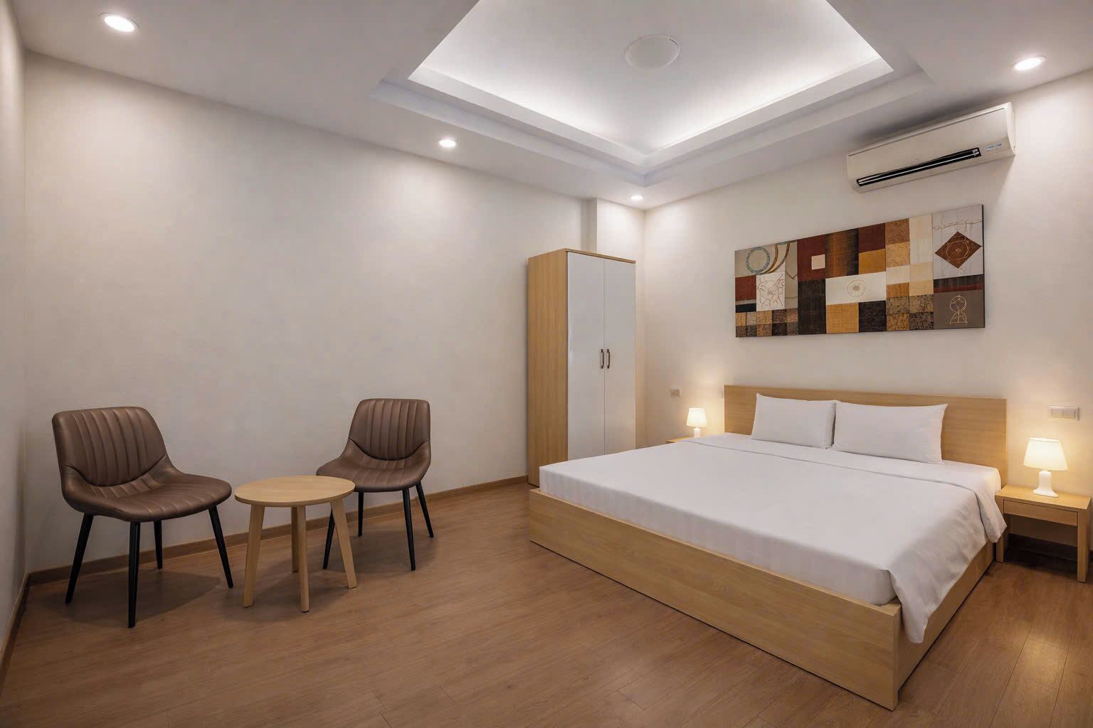 A hotel room with a bed, two chairs, a small table, a wardrobe, and a ceiling light.