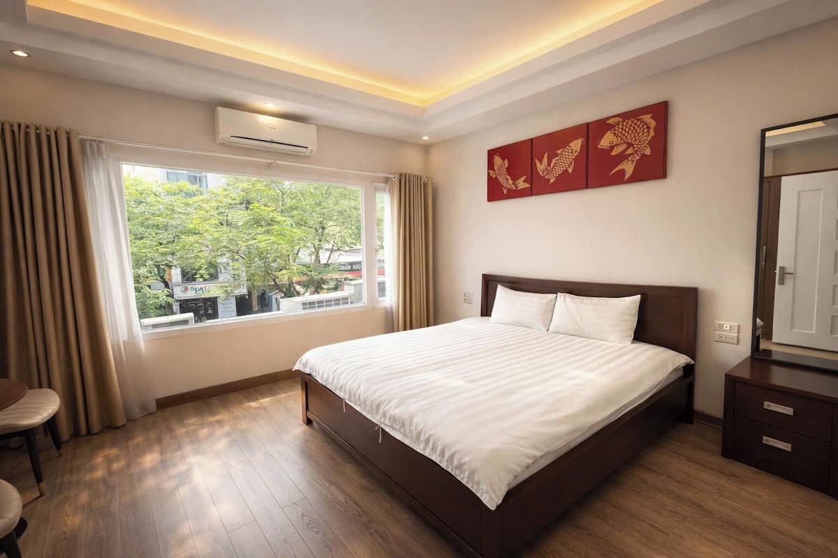 Une chambre d’hôtel avec un grand lit, une fenêtre avec des rideaux, un appareil de climatisation et un mur décoré de peintures représentant des poissons.