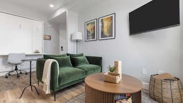 A modern living room with a green sofa, a round wooden coffee table, and a flat-screen TV mounted on the wall.