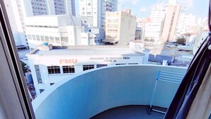 A view from a balcony with a cityscape in the background, including a building with 'FMU' and 'FACULDADE DE EDUCAÇÃO FÍSICA PRÉRIO 20' signage. - APARTAMENTO O PREFERIDO LIBERDADE SP (São Paulo)