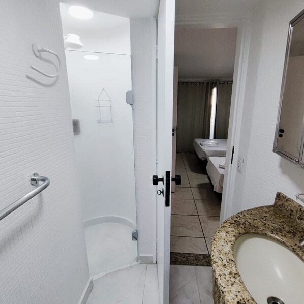 A bathroom with a white tiled wall, a shower area, a sink with a granite countertop, and a mirror. - APARTAMENTO O PREFERIDO LIBERDADE SP (São Paulo)