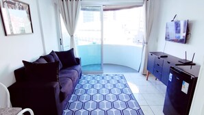 A living room with a sofa, a dining area with a table and chairs, a kitchen area with cabinets and appliances, and a view through a glass door to the outside. - APARTAMENTO O PREFERIDO LIBERDADE SP (São Paulo)