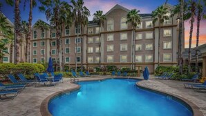 Un hotel con piscina circondata da poltrone a sdraio e palme.