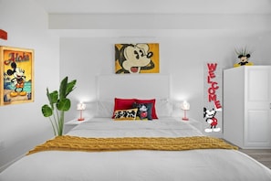 Une chambre à coucher comprenant un lit, des oreillers, une table de chevet, une lampe, une plante et des éléments de décoration murale, notamment un tableau et un panneau.