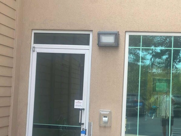 A building facade with a glass door and window, a security intercom, and a sign indicating a 24-hour reception.