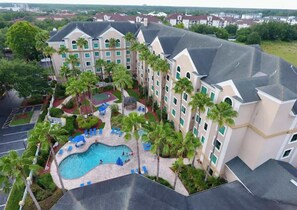 A hotel with a swimming pool, palm trees, and a tennis court.