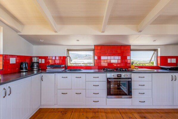 Una cocina moderna con armarios blancos, salpicadero rojo y un amplio ventanal con vistas a la vegetación.